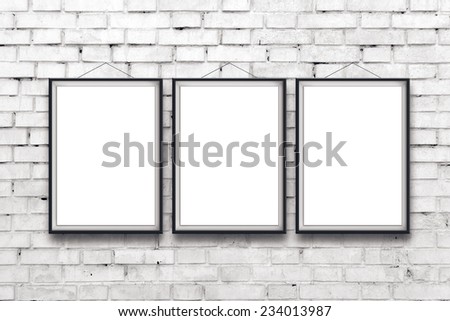 Three blank vertical painting poster in black frame hanging on white brick wall. Painting proportions match international paper size A.