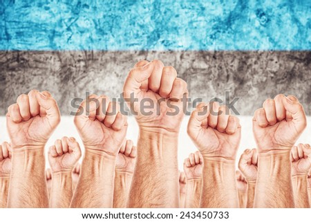 Estonia Labor movement, workers union strike concept with male fists raised in the air fighting for their rights, Estonian national flag in out of focus background.