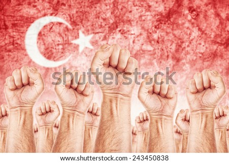 Turkey Labor movement, workers union strike concept with male fists raised in the air fighting for their rights, Turkish national flag in out of focus background.