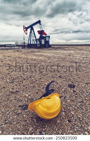 Protective Hardhat and Pumpjack Oil Pump operating on natural gas in the field pumping from the oil well.