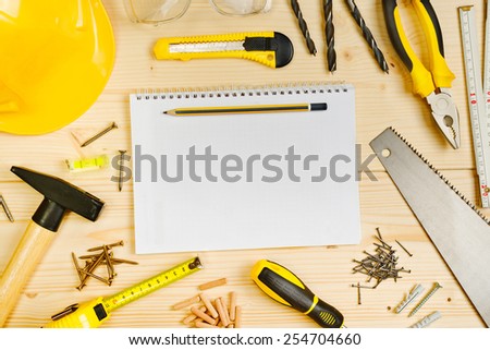 Top View of Planning a Project in Carpentry and Woodwork Industry Concept, Notebook and Assorted Woodwork and Carpentry Tools on Pinewood Workshop Table.