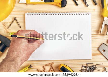 Top View of Planning a Project in Carpentry and Woodwork Industry, Notebook and Assorted Woodwork and Carpentry Tools on Pinewood Workshop Table.