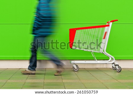 Motion Blur Man Walking by Empty Shopping Cart Trolley in front of a Shopping Mall as Consumerism Concept Background.