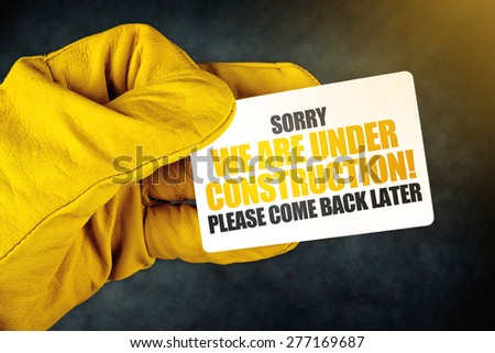 Under Construction on Business Card, Male Hand in Yellow Leather Construction Working Protective Gloves Holding Card with Rounded Corners.