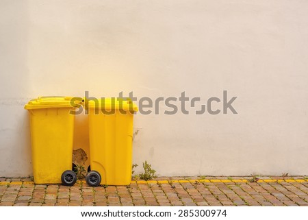 Two Yellow Plastic Recycle Bins on the Street Against Blank White Wall as Copy Space for Text, Toned Image