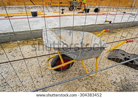 Empty Industrial Handcart on Construction Site, Dirty Wheelbarrow with Worker in Background
