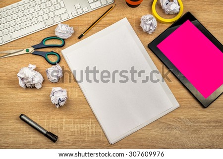 Graphic designer tabletop workspace with computer keyboard, digital tablet pc, blank drawing paper sheet, pencils, scissors, crumpled paper, top view overhead shot.