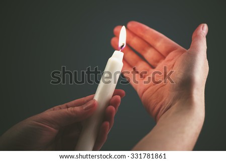 Female hands with burning candle in the dark, woman lighting up the candle as religious ceremony