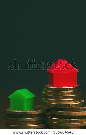 Home mortgage concept with small arrow-shaped plastic house models on top of stacked coins.
