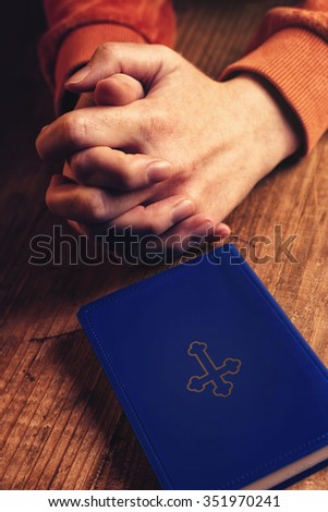 Christian woman praying with hands crossed and Holy Bible by her side on wooden desk in church