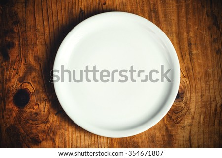 Empty white dinner plate on rustic wooden kitchen table, top view