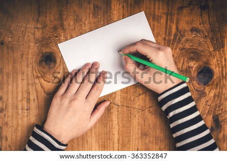 Woman writing recipient address on mailing envelope, female hands from above on office desk sending letter, top view, retro toned.