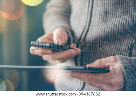 Smartphone and tablet data synchronization, man syncing files and documents on personal wireless electronic devices at home, selective focus with shallow depth of field and bokeh light.