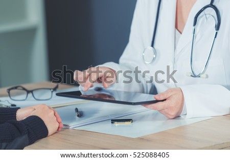 Female doctor presenting medical exam results to patient using digital tablet computer in hospital office.