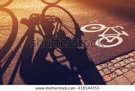 Shadow of unrecognizable cyclist riding a bike on bicycle lane through city street next to the road marking in urban surrounding, retro toned