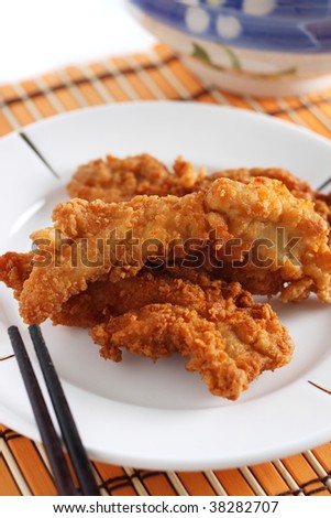Fried chicken pieces on white plate over bamboo mat.