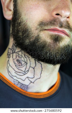 Bearded hipster handsome tattooed man. Rose tattoo on her neck