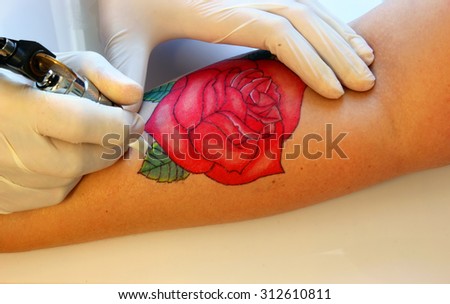 Tattooer showing process of making a tattoo on young  woman hand. Tattoo design in the form of rose
