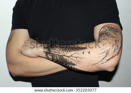 Portrait of young hipster man with tattooes on his hand. Tattoo design in the form eagle and dark forest. - Stock Image - Everypixel