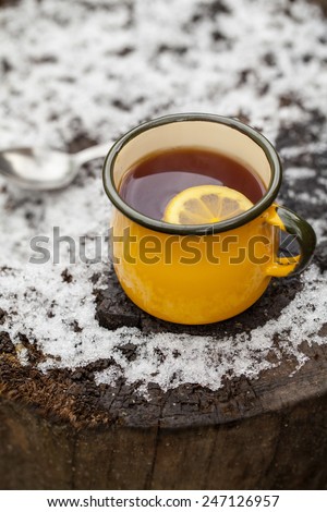 Mug of hot tea with lemon on frozen tree trunk
