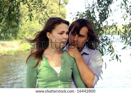 Romantic portrait of young couple against river and trees
