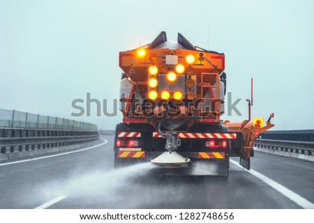 Orange highway maintenance gritter truck spreading de-icing salt on road in winter.