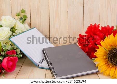Notepad and flower on wood texture.