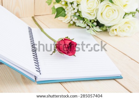 Red rose flower and Notepad book on wood texture.