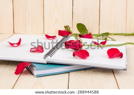 Red rose flower and Notepad book on wood texture.