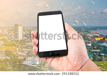 Man hand hold blank touch screen smart phone on rain drops on a window or water drops on grass blurred with cityscape background.