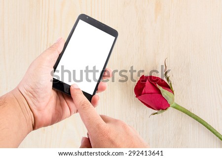 Man hand hold blank touch screen smart phone on background with red roses on wood texture for background.