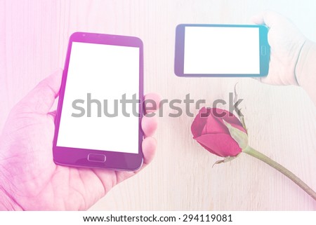 Man hand hold blank touch screen smart phone on background with red roses on wood texture for background. with pink and blue color filter.