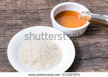 pouring sesame seeds oil in bowl and white sesame seeds in plate on wooden table top