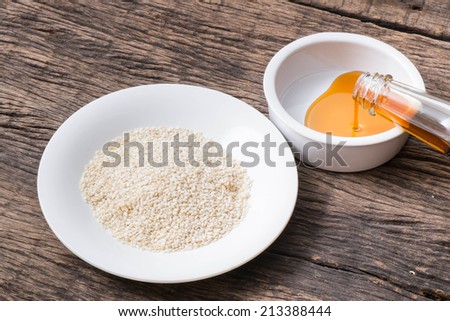 pouring sesame seeds oil in bowl and white sesame seeds in plate on wooden table top