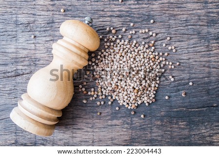 white peppercorns and wooden pepper shaker on wooden table top