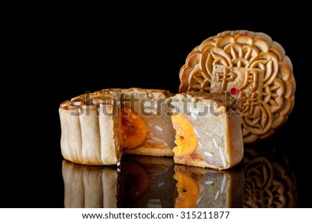 Two moon cake with one cut up to show egg yolk for the chinese Mid-Autumn festival on wooden table top and wooden background