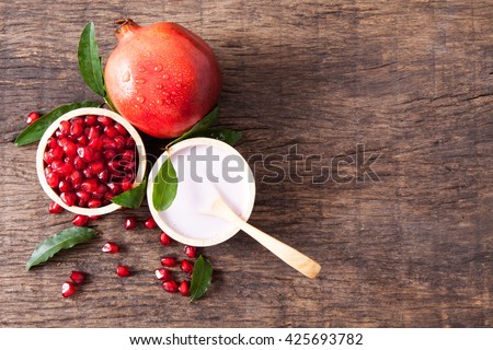 Top view of lotion in bowl with fresh pomegranate seeds on wooden table top