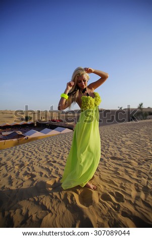 White blonde girl in green dress alone in arabic desert. blue sky.