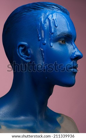 Portrait of a man poured blue paint on a pink background