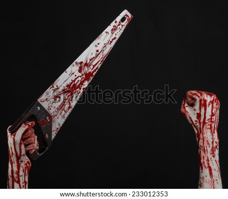 Halloween theme: bloody hand holding a bloody saw on a black background