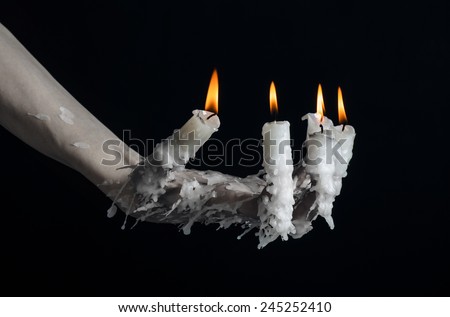 Halloween theme: on the hand wearing a candle and dripping melted wax on black isolated background
