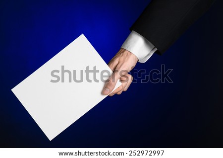 Business and advertising topic: Man in black suit holding a white blank card in his hand on a dark blue background in studio isolated