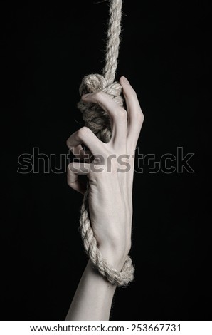 Suicide and depression topic: human hand hanging on rope loop on a black background
