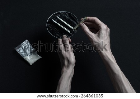 The fight against drugs and drug addiction topic: addict hand holds a mirror with strips of cocaine and drugs around her lie on a dark background, top view in the studio
