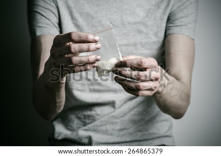 The fight against drugs and drug addiction topic: addict holding package of cocaine in a gray T-shirt on a dark background in the studio