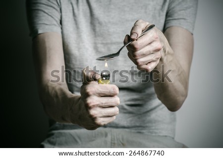 The fight against drugs and drug addiction topic: addict holding spoon lighter and heats the liquid drug in a T-shirt on a dark background