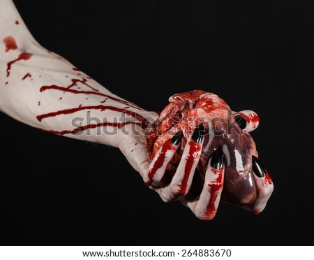 Bloody horror and Halloween theme: Terrible bloody hands with black nails holding a bloody human heart on a black background isolated background in studio