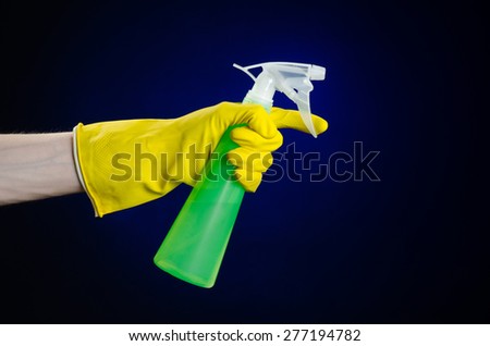 Cleaning the house and cleaner theme: man\'s hand in a yellow glove holding a green spray bottle for cleaning on a dark blue background in studio