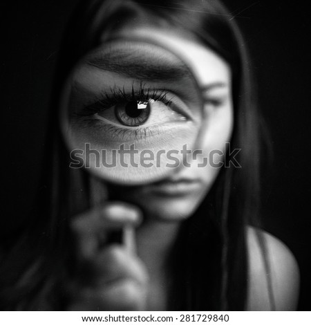 A girl holding a magnifying glass on a dark background, scary big eyes