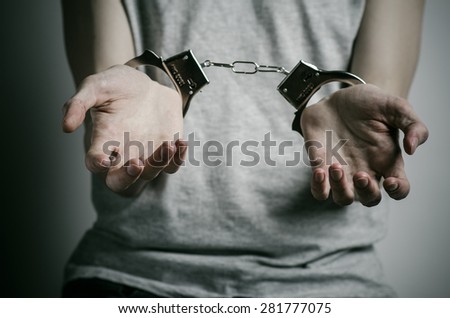 Prison and convicted topic: man with handcuffs on his hands in a gray T-shirt on a gray background in the studio, put handcuffs on rapist